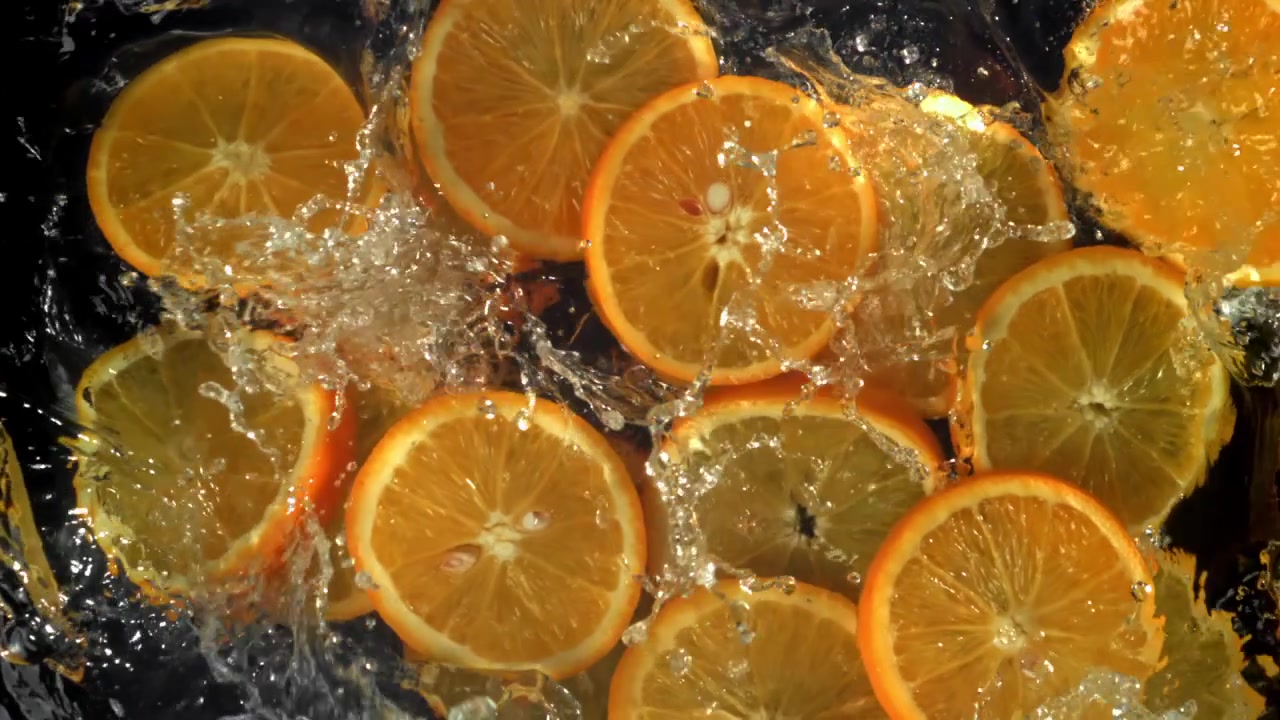 Fette d'arancia fresche che schizzano nell'acqua al rallentatore