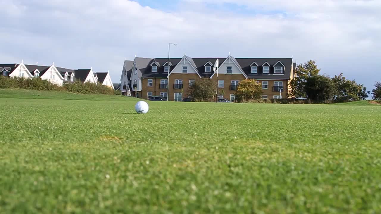 Ground level shot of a golf ball on the green. Golfer shadow seen as they walk past.