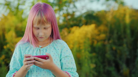 the child uses a smartphone the girl with pink hair and a pink phone in her hands