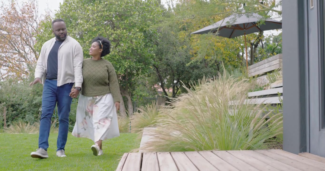 African couple starting backyard stroll, holding hands and walking toward wooden deck, talking