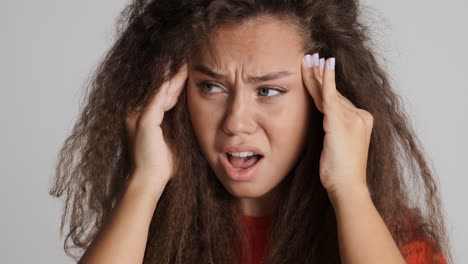 mujer caucásica de cabello rizado con dolor de cabeza frente a la cámara.