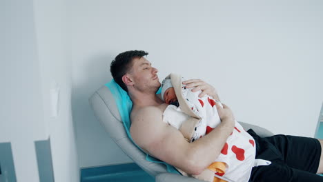 caucasian mid-aged man lies on a bed in hospital. father holds his child on the chest after labor.