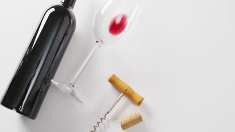 Red-wine-bottle,-empty-glass,-cork-and-corkscrew-lying-on-white-surface-with-copy-space