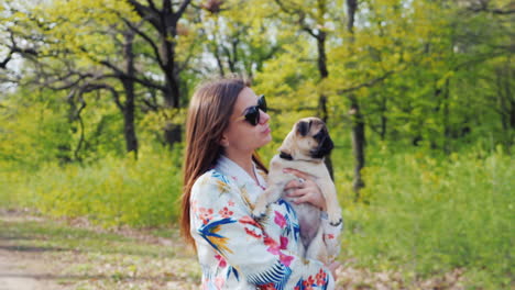 young stylish woman in sunglasses walking in the park with a dog of pug breed