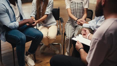 Primer-Plano:-Un-Hombre-Con-Barba:-Un-Psicólogo-Entrevista-A-Participantes-De-Terapia-De-Grupo-Que-Están-Sentados-En-Círculo-Y-Escribe-Sus-Pensamientos-En-Su-Tableta-Usando-Un-Bolígrafo