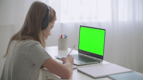 El-Aprendizaje-Electrónico-Para-Escolares-Por-Parte-De-Una-Chica-De-Internet-Está-Dibujando-En-Un-Cuaderno-Que-Escucha-A-Un-Maestro-Mediante-Una-Pantalla-Verde-De-Videochat-En-Una-Computadora-Portátil