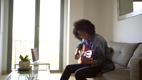 positive black woman playing guitar at home