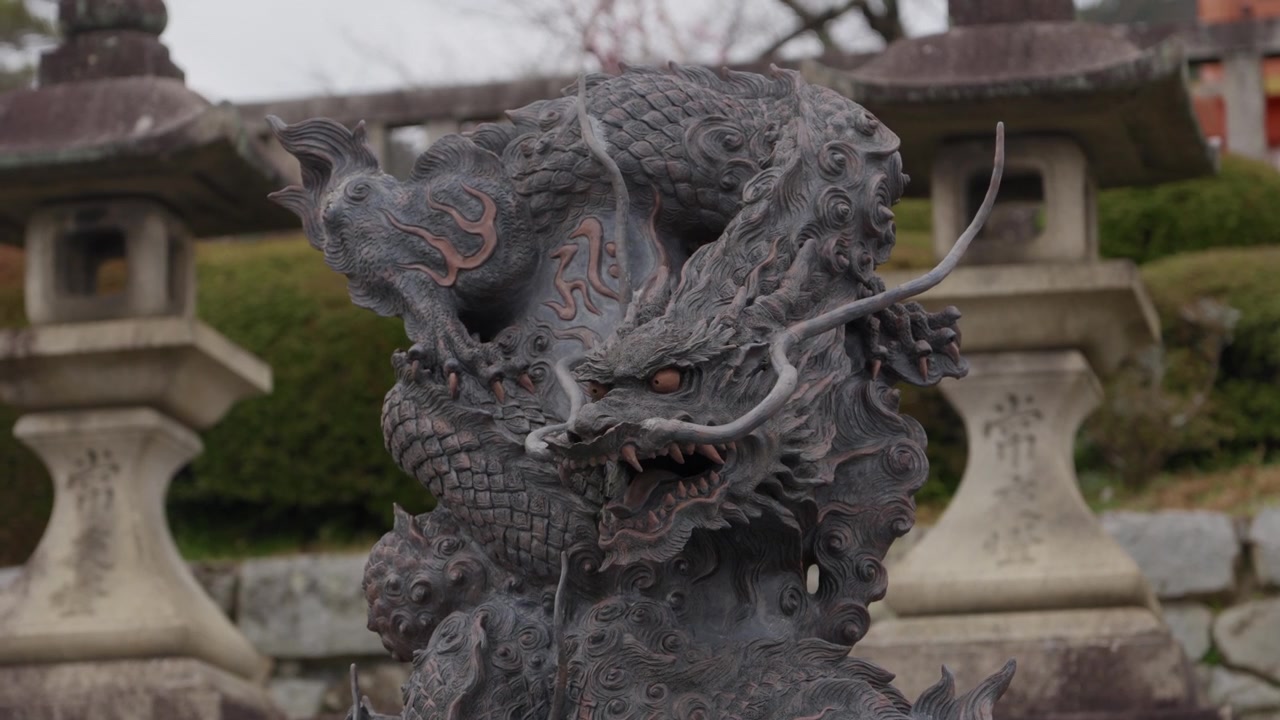 Statua di drago in bronzo ornata su una fontana di purificazione temizuya in pietra tra lanterne di pietra in un santuario giapponese.