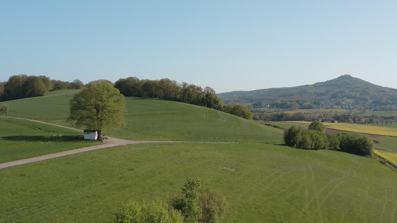 Drone - Aerial panorama shot of al lonely chapel on a field with grass and a road with an tractor and a panorama of the seven mountains - Siebengebirge 25p