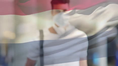 Animation-of-flag-of-netherland-waving-over-man-wearing-face-mask-during-covid-19-pandemic
