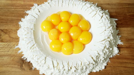 top view of pasta making: perfect egg yolks are poured inside a well of flour