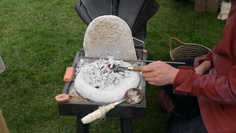 Viking-blacksmith-at-work-with-a-small,-portable-forge,-focusing-on-metal-craft-against-a-natural-backdrop