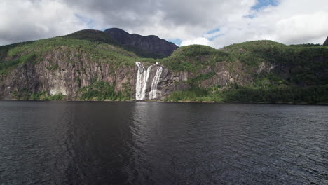 Camera-pans-slow-and-low-over-Setenesfjorden,-centred-upon-the-majestic-Laukelandsfossen-waterfall-in-the-distance