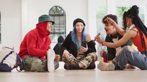 Happy-diverse-male-and-female-dancers-talking-and-using-smartphone-in-dance-studio,-slow-motion