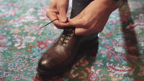 caucasian man's hands tying his brown leather dress shoe laces on his right foot wearing a watch