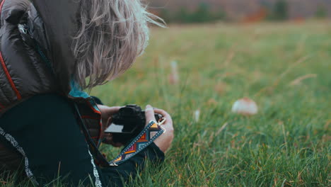 close up shot of a woman with grey hair from behind lying on the grass and taking photos of a mushroom in nature during a cold windy day in autumn