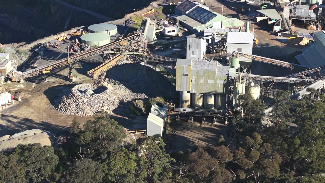 Filmato cinematografico con drone cattura i macchinari robusti e i cumuli di aggregati della Cava di Montrose a Melbourne, illuminati dalla luce naturale del giorno. Impianto industriale, nastri trasportatori e bordo della foresta visibili. Nessuna persona.
