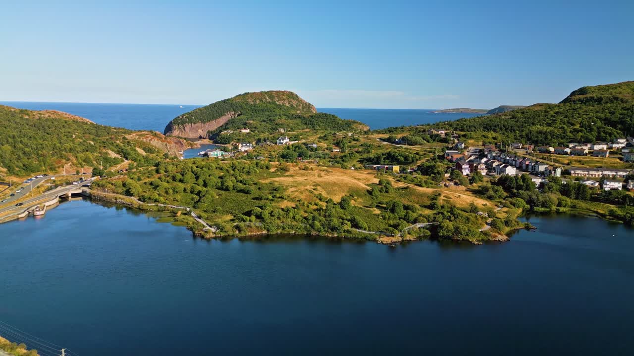 A drone soars over Quidi Vidi's rugged headland, capturing the contrast between the rocky hills and the vivid blue waters of the harbour and Atlantic