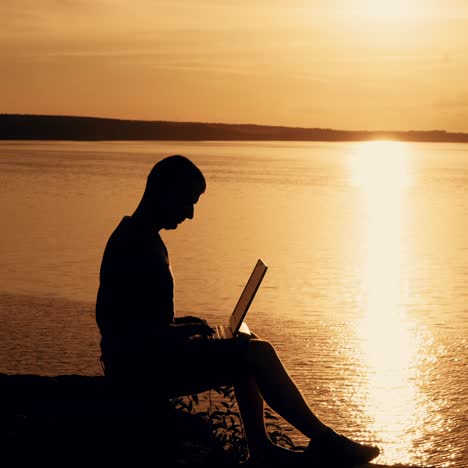 man sit and work on the laptop by sunset (sunrise) background on the top of the hill