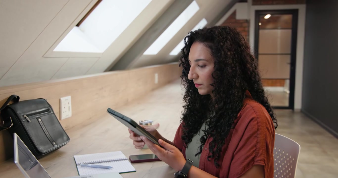 African American woman rust top typing on laptop pausing to scan charts tapping tablet at desk