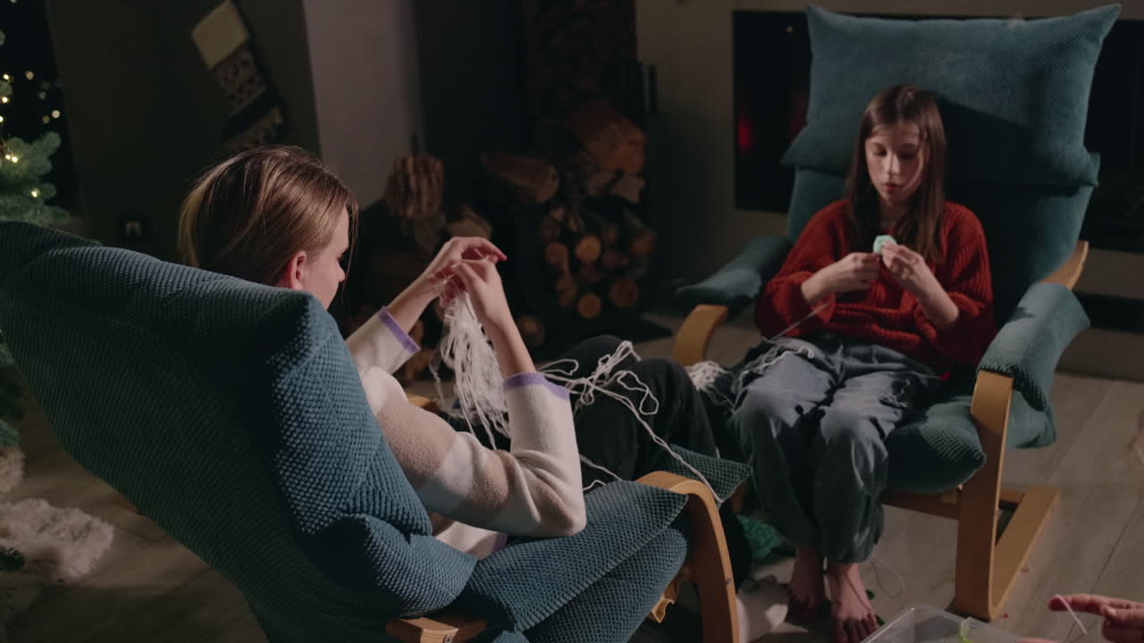 Two girls knitting by the fireplace at home during Christmas