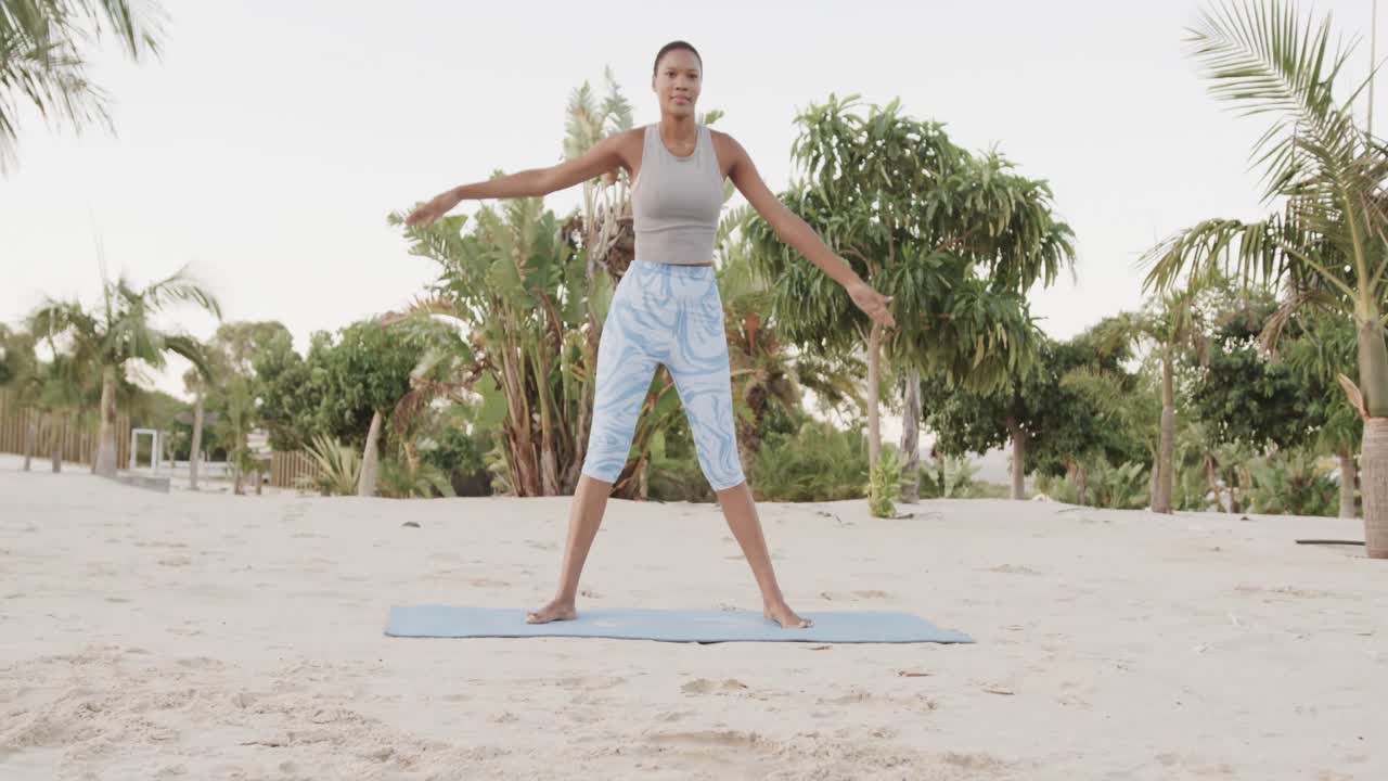 mujer biracial feliz practicando yoga de pie en la playa, cámara lenta