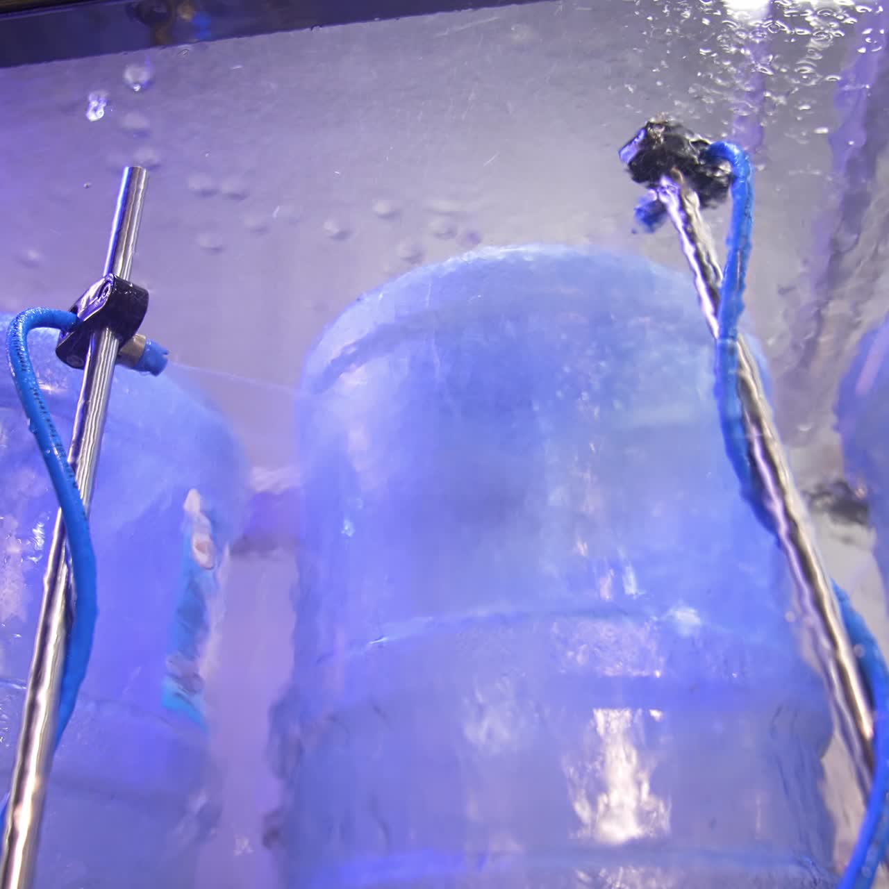 Blue big bottles are put upside-down and being washed. Flasks are sprayed with water for cleaning. Low angle view