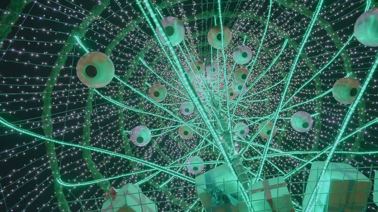 The Above View Of A Giant Christmas Tree With Hanging Round Lanterns, Small Gifts, And Christmas Lights During Evening - Close Up Shot