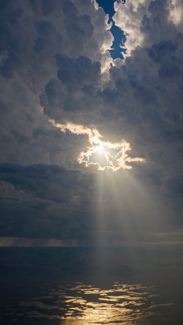 Dramatic aerial video shot of towering clouds with sun rays breaking through, casting reflections