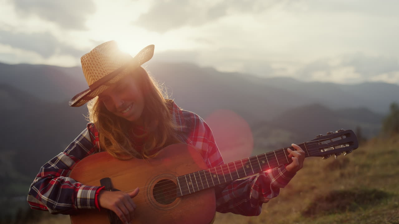 un músico sonriente interpreta una canción en la guitarra de cerca. una mujer toca en las montañas.