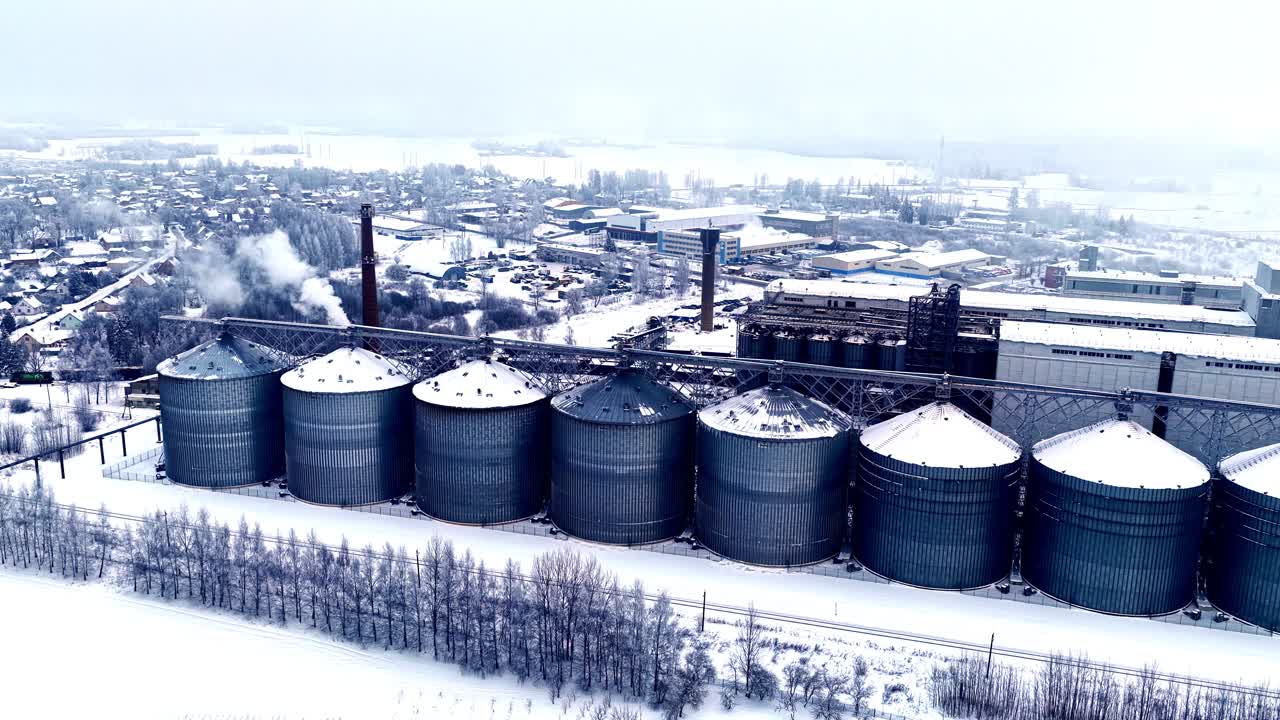 Industrielle Bottiche und ein Schornstein neben kleinen Vorstadthäusern in einer verschneiten Winterlandschaft, Luftaufnahme fährt nach rechts