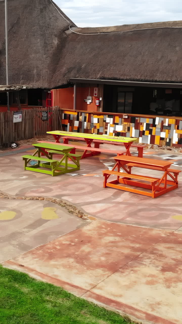 Área de pátio externo vibrante com mesas de piquenique coloridas e murais artísticos