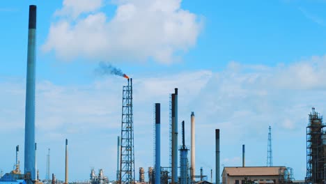 slow motion wide angle shot of a large industrial refinery with black, polluting smog pouring out into a clear blue sky in curacao