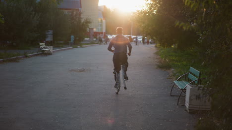 man running on stilts along quiet residential street during sunset, captured from behind. he is wearing dark sweater and pants, with warm sunlight highlighting the tranquil outdoor scene