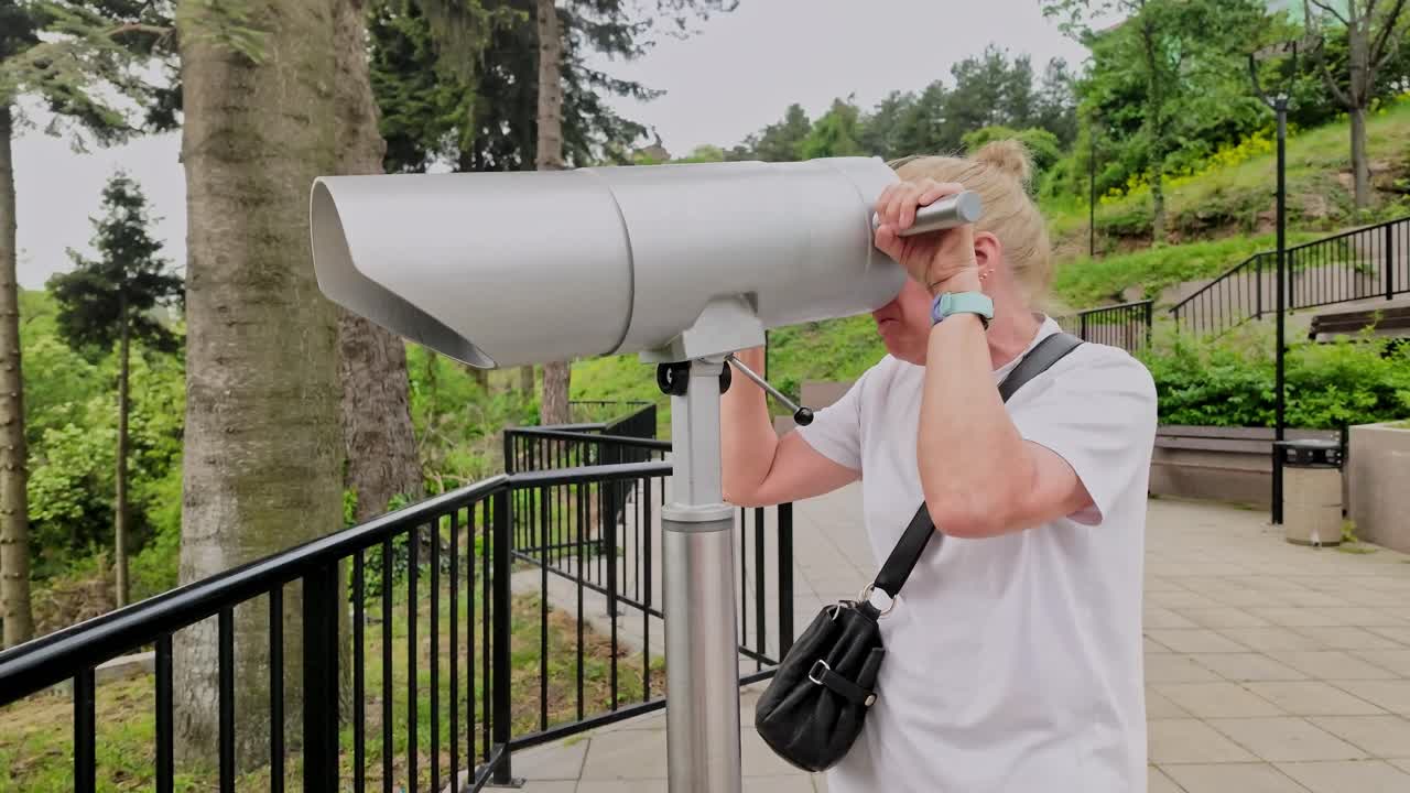 mujer mira a través de un telescopio en un punto de observación panorámico