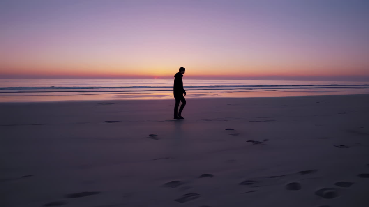 Silhouette of a person walking on a beach at sunset/sunrise