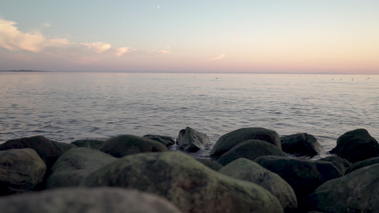 una toma panorámica desde una costa rocosa sobre el mar durante la puesta de sol en cámara lenta