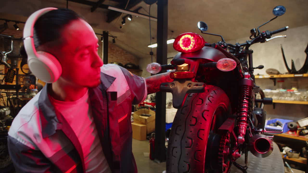 Male Specialist Listening to Music in Headphones while Repairing Motorbike
