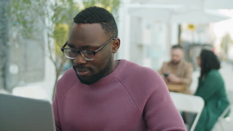 african american man using laptop in outdoor cafe