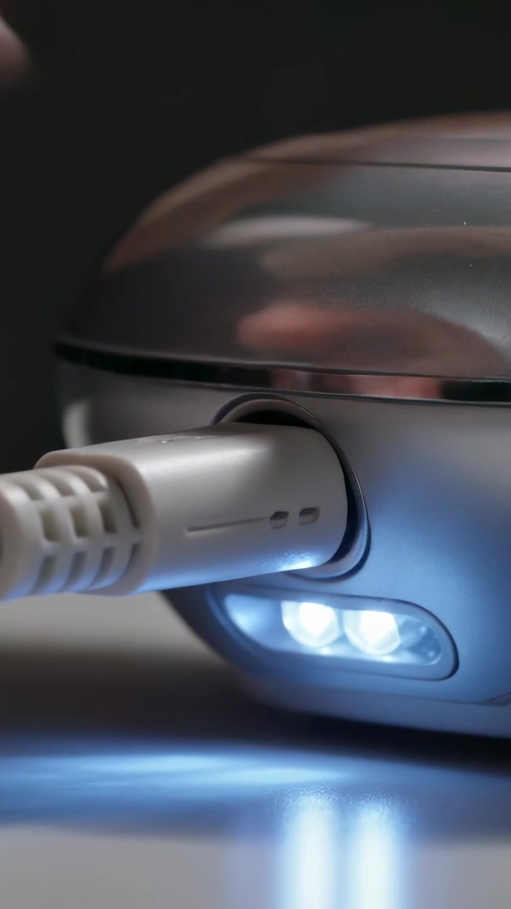 Vertical video: Grasping hand inserting metal plug into gray device port on desk, lighting oval LED
