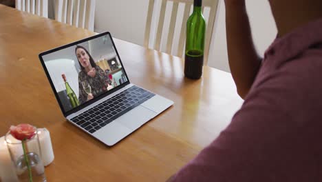 Mid-section-of-african-american-man-drinking-wine-while-having-a-video-call-on-laptop-at-home