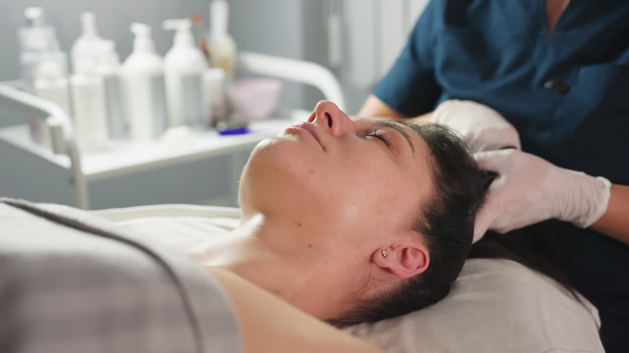 Beauty technician wearing gloves packs client hair with white cloth during spa session in modern treatment room showcasing professional care hygiene comfort and promoting relaxation