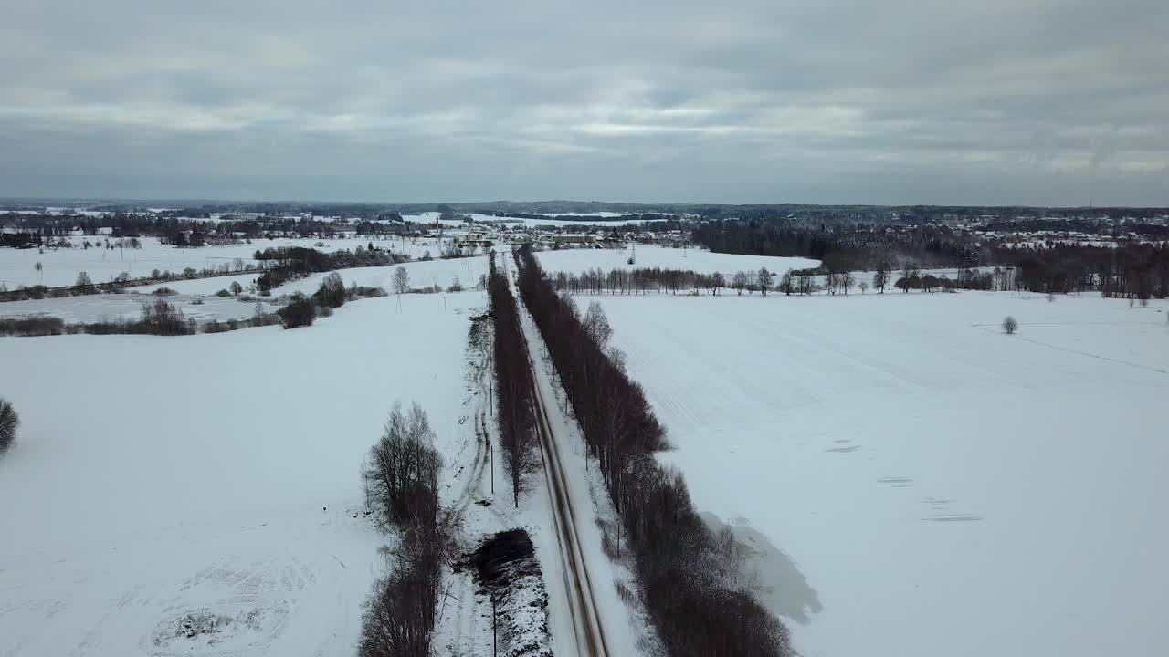 겨울의 흐린 날 자작나무 골목 한가운데 눈 덮인 도로 위를 천천히 날아가며 멀리 눈 덮인 도시 풍경