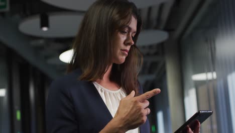 mujer de negocios caucásica con cabello marrón usando una tableta en una oficina moderna