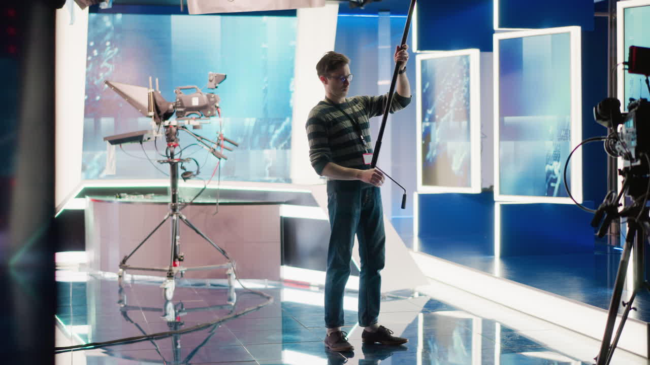 Studio technician in modern broadcast studio setting adjusting equipment with boom pole, looking up while preparing for shot. Focus on professional media production environment and technology