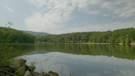 woodland landscape with calm lake and reflections of cloudy blue skies