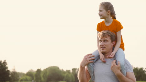 happy father carrying his smiling daughter on shoulders in a park while walking and talking to her