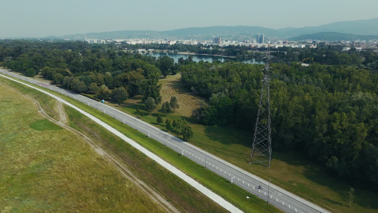 aerial - power line tower near bike path and forest with Sava River and Zagreb city skyline