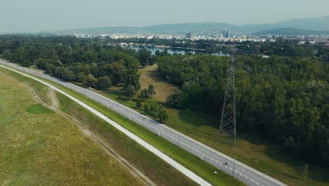 aerial - power line tower near bike path and forest with sava river and zagreb city skyline