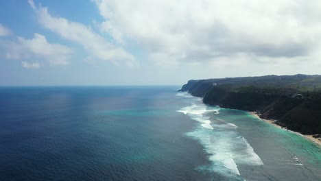 Fantastische-Meereslandschaft-Aus-Der-Luft-Mit-Klippen-Und-Weißem-Sandstrand,-Blauen-Ozeanwellen-Und-Dramatischen-Wolken-Am-Blauen-Himmel